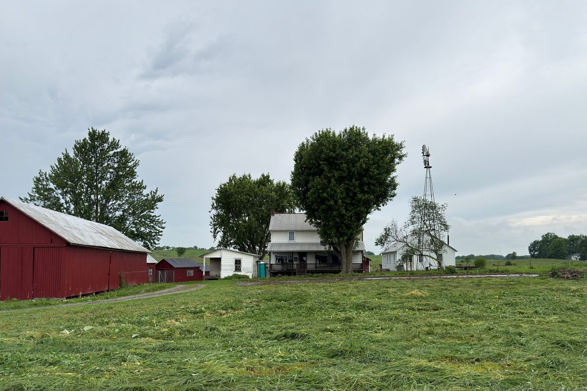 Red barn, white farmhouse and a metal windmill tower beside a mowed field