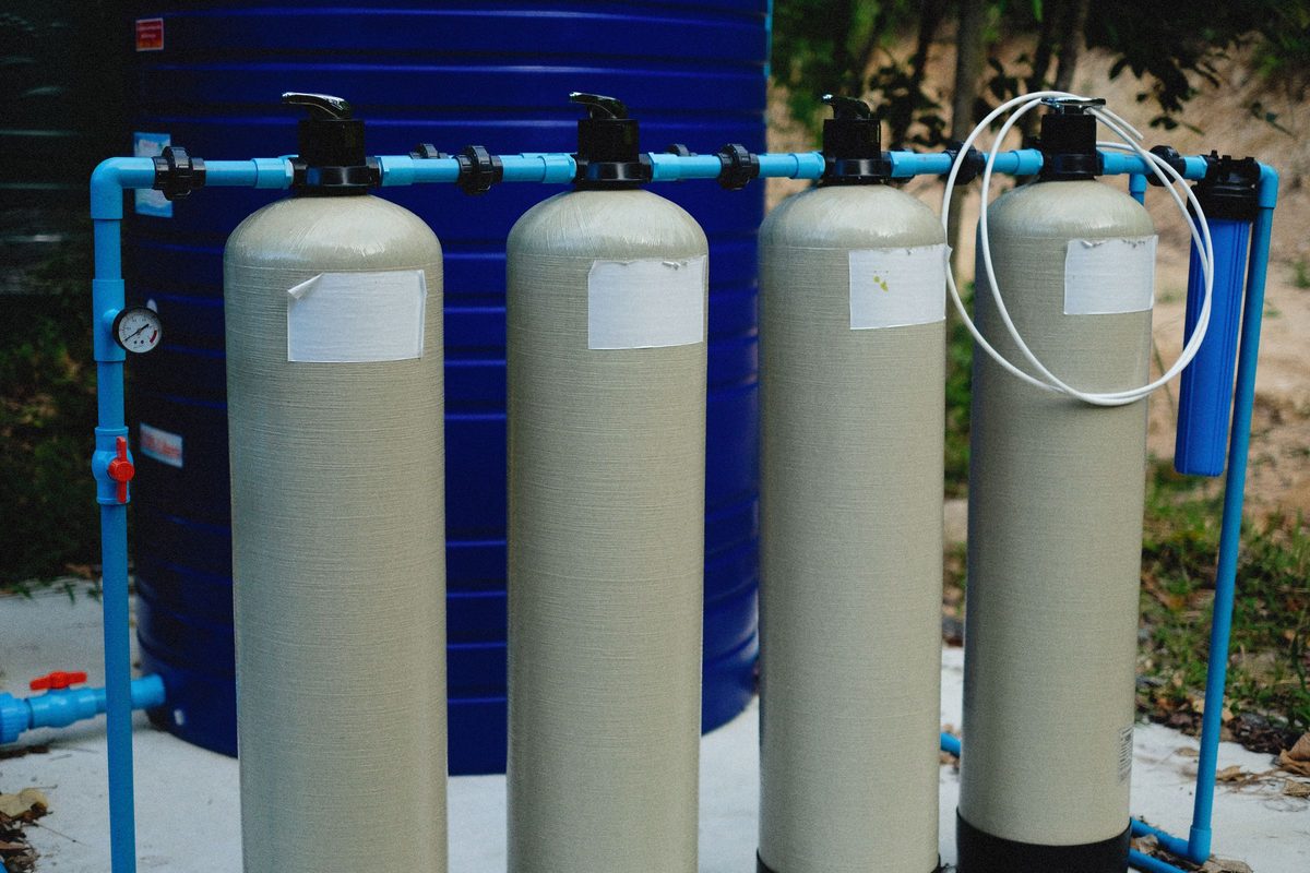 Four fiberglass water treatment tanks joined by blue PVC pipe with a pressure gauge