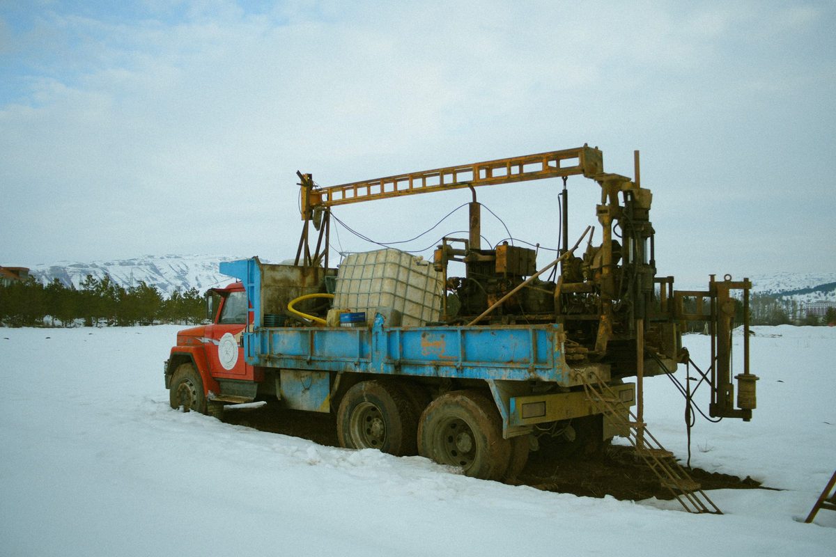 Truck-mounted drilling rig with a mast and water tank parked in a snowy field
