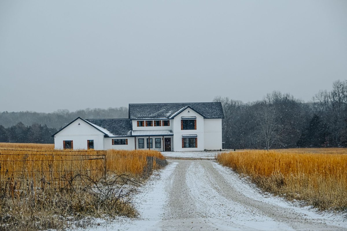 White farmhouse at the end of a gravel drive between fields