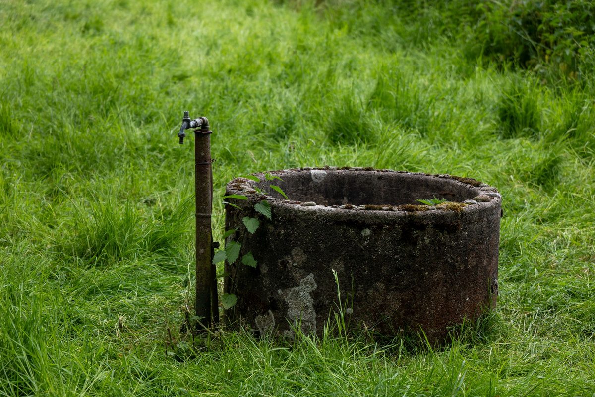 Old round stone well with a metal tap in a grassy field